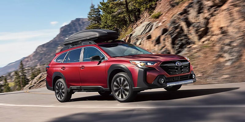 Red Subaru Outback driving on a mountain highway with a black cargo box mounted on the roof