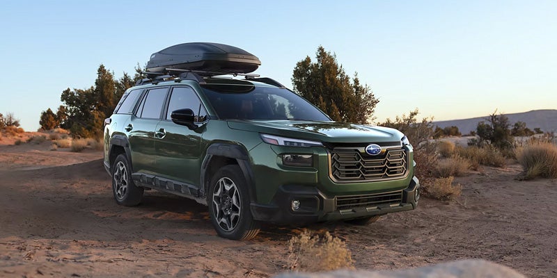 Green Subaru SUV parked on a desert trail with a roof cargo carrier, showcasing adventure-ready capability