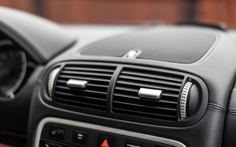 Close-up of a car's black dashboard with two horizontal air vents and a speaker grill