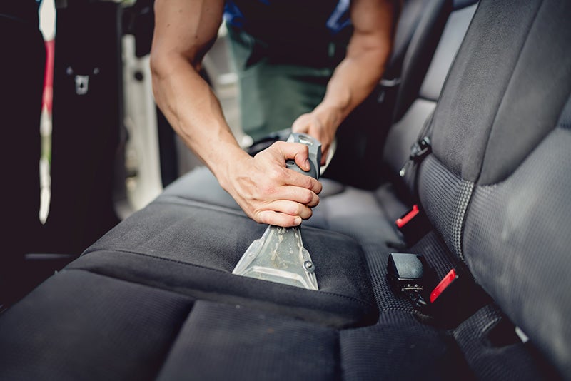 Person using an upholstery extraction tool to deep-clean a fabric rear car seat