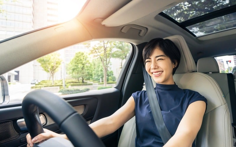 The image shows the interior of a modern vehicle during daytime. A person is seated in the driver's seat