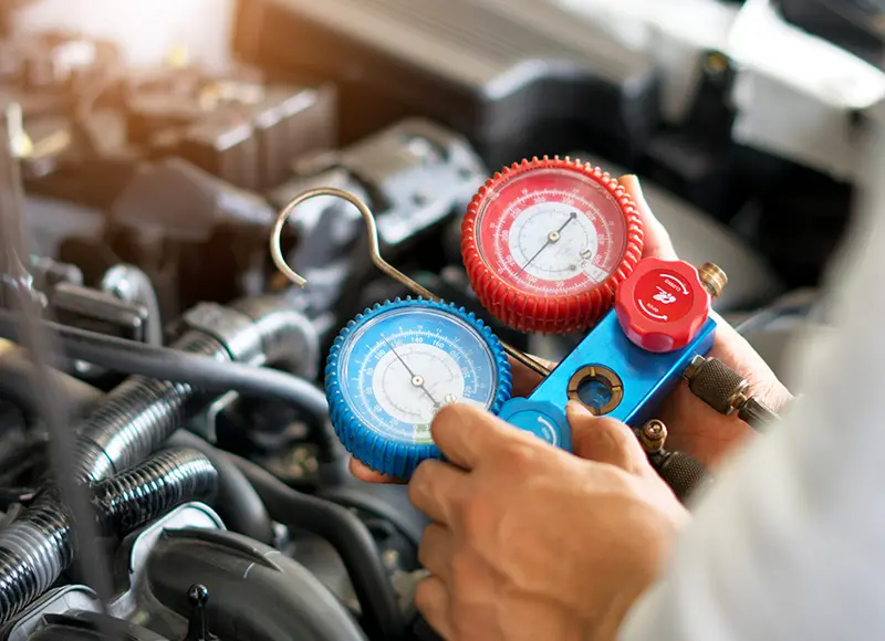 A technician is holding a manifold gauge set with blue and red pressure gauges