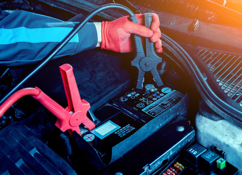 Technician connecting testing equipment to a vehicle battery during battery inspection and maintenance