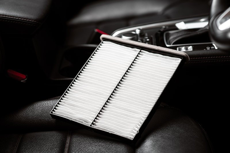 A clean rectangular pleated air filter is placed on a vehicle seat inside the cabin