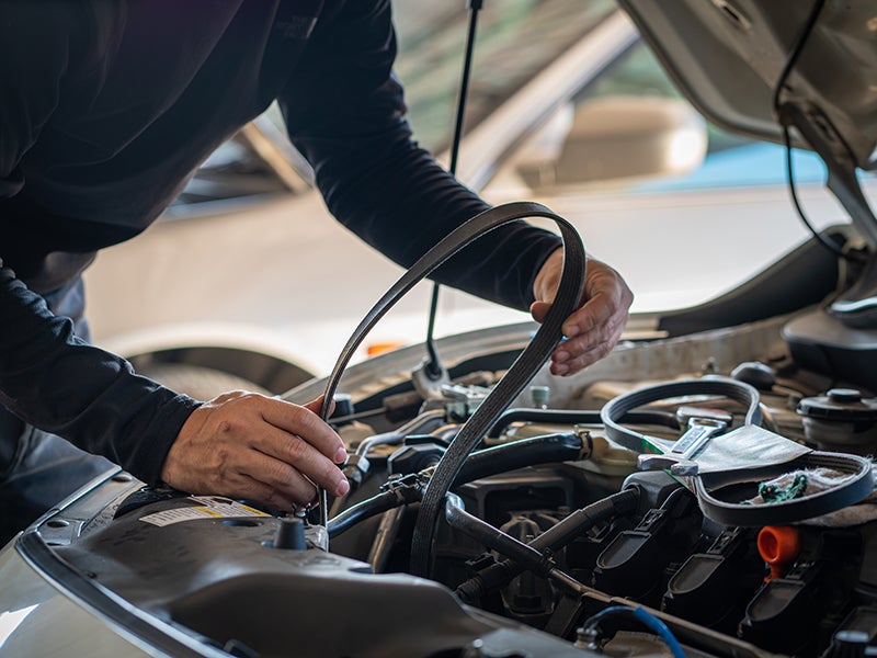 A mechanic's dirty hands holding a serpentine belt above an open car engine