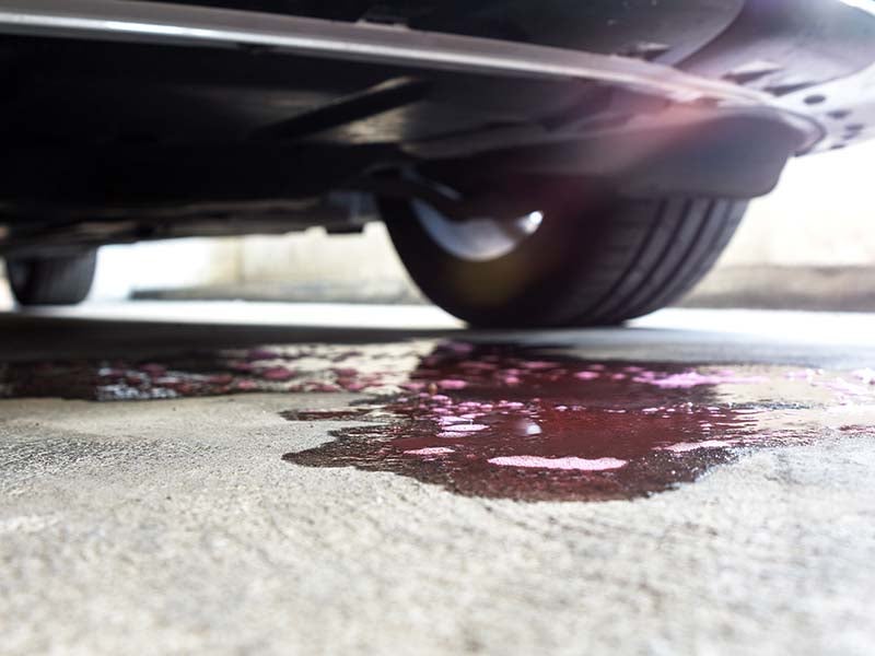 Puddle of red automotive fluid leaking from underneath a parked vehicle onto pavement