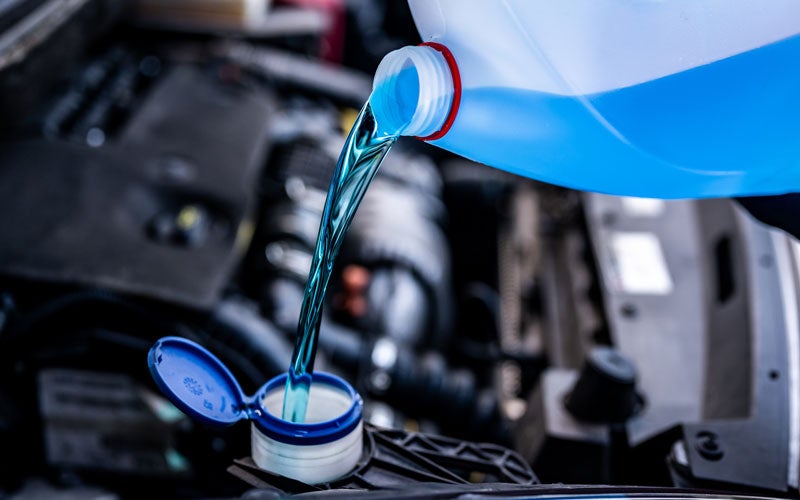Blue windshield washer fluid being poured into a vehicle's washer fluid reservoir under the hood