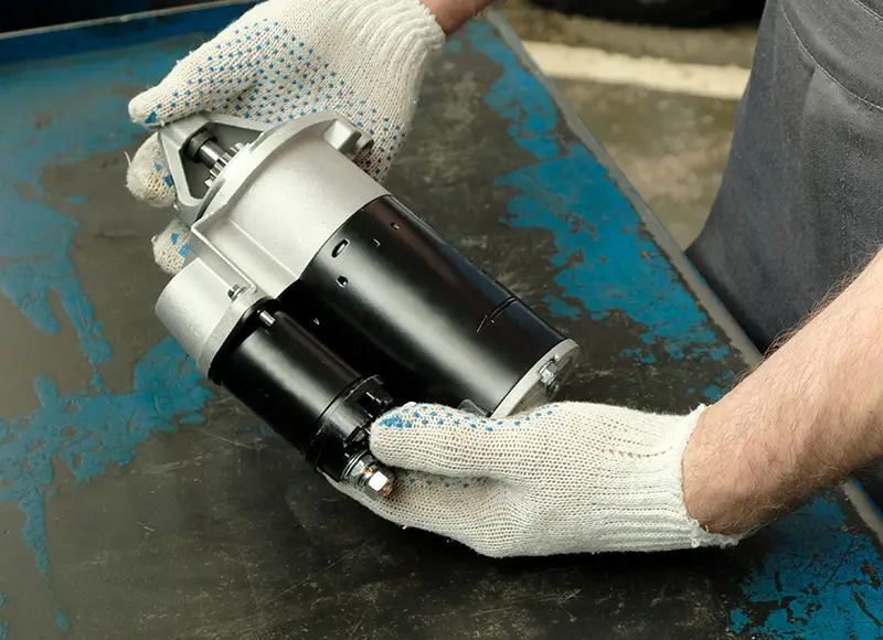 A close-up of a vehicle starter motor or a similar automotive electrical component placed on a workbench