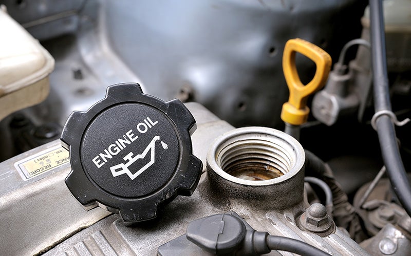 Open engine oil filler cap and oil fill port on a vehicle engine, with the oil dipstick visible nearby