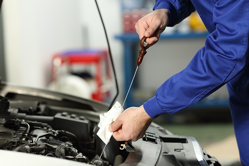 Technician checking engine oil level with a dipstick in a vehicle engine compartment