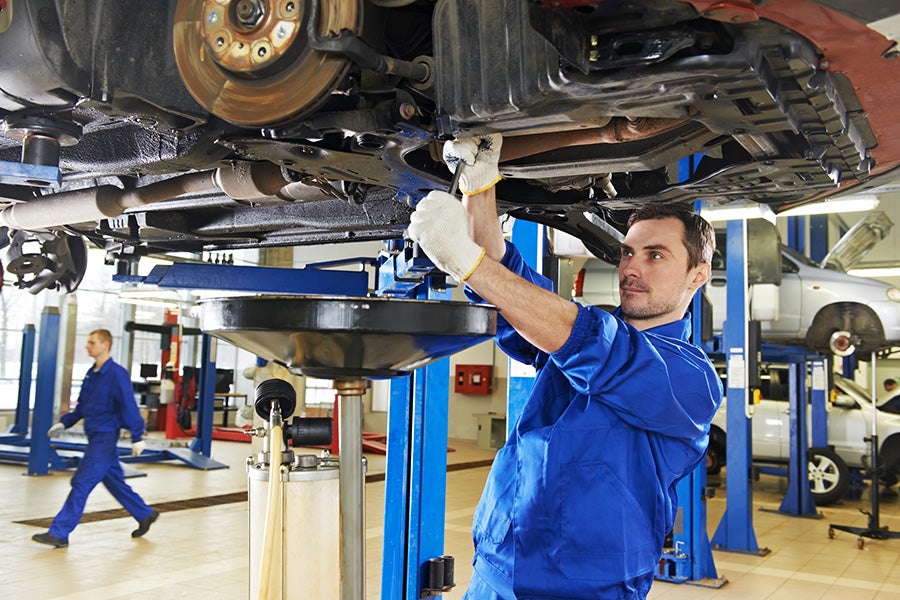 A technician wearing a blue work uniform and protective gloves is working beneath the vehicle