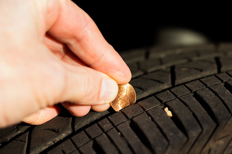 Hand inserting a coin into a vehicle tire tread to check tread depth and tire wear