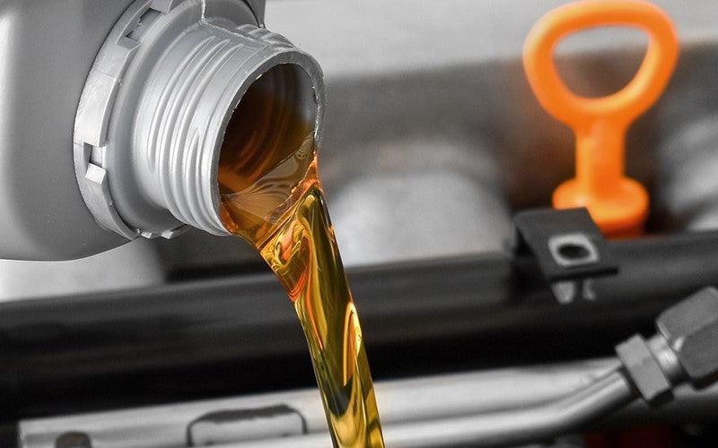 Fresh engine oil being poured into a vehicle engine through the oil filler opening